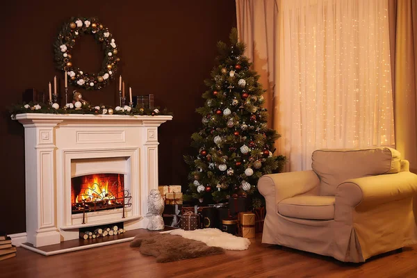Warm and cozy evening in Christmas room interior design, Xmas tree decorated by lights presents gifts toys, candles, garland lighting indoors under the fireplace. Holiday living room.New year holidays