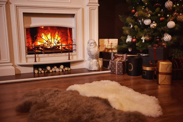 Winter holidays atmosphere in a warm room with a christmas tree full of lights and toys near a cute fireplace with fire and present toys. Christmas interior. New year design