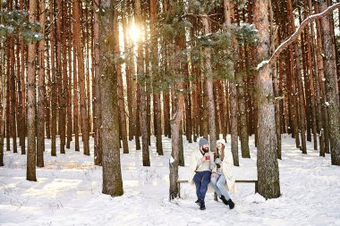 Sıcak kış tatilleri doğada ve köyde, kırsalda, sıcak içecekler ve insan konsepti. Ormanda günbatımı geçmişi olan mutlu, genç bir çift. Kış tatili konsepti. Kış tatili.