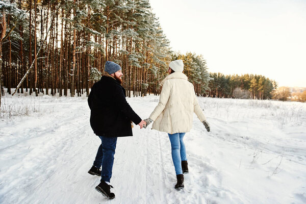 Funny couple emotionally runs in the winter woods. Full-length Horizontal Back View. Christmas vacation together. Outdoor seasonal activities. Winter holiday lifestyle romantic relationship concept.