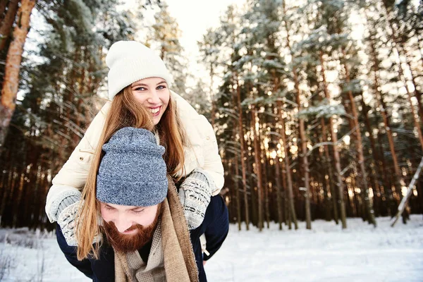 Man giving woman piggybacks ride on winter vacation in a snowy forest. Background with text space for your promotion or website about traveling during the cold season. Winter holiday activity concept