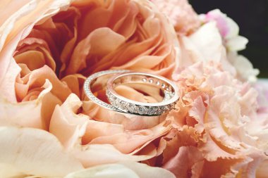 Bir çift platin alyans. Çiçekli arka planda beyaz altın alyansların yakın çekimi. Elmaslı gelin yüzüğü. Sığ odak