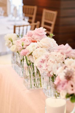 Yeşillik ve beyaz ve pembe çiçekleri yeni evliler için düğün masasında sergiliyorum. Masada beyaz kumaşlı güzel çiçekler, boş alan. Dikey fotoğrafçılık