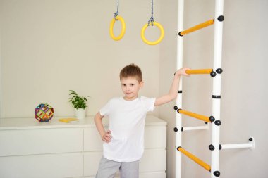 Çocuk kameranın önünde poz veriyor, çerçeveye bakıyor. Evin spor köşesi. Genç yaştan itibaren sağlıklı yaşam tarzı kavramı. Spor, sağlıklı yaşam tarzı, evde boş vakit geçirme.