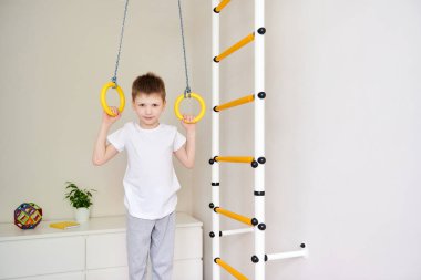 Çocuk kol kaslarını çalıştırıyor. Spor giyimli genç bir çocuk duvarlarda spor yüzükler takıyor. Genç yaştan itibaren sağlıklı yaşam tarzı kavramı. Çocuk sporu.