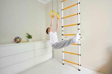 Çocuk ellerini tutar ve fiziksel egzersizler yapar bacaklarını dik açıyla kaldırır, korteks kaslarını çalıştırır. Fiziksel, duyusal, motor becerileri geliştirme, ev egzersizi konsepti. Spor.