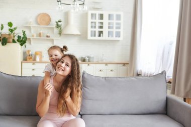 Uzun kıvırcık saçlı, güzel annesinden küçük kız kucaklaşması. Evdeki kanepede kucaklaşarak eğlenin. Hafta sonu boş zamanlarının, bağ kurma konseptinin tadını çıkar. Anneler Günü aile babalığını sever..