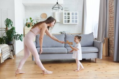 Heyecanlı anne ve küçük kız dans ediyor ve evdeki rahat oturma odasında mutfak aletleriyle oynuyor, aile mutfakta çıplak ayakla gezerken eğleniyor. Birlikte zaman geçirme kavramı.