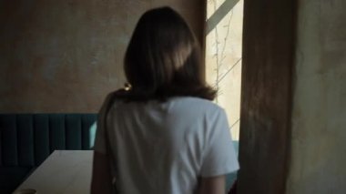 Beyaz tişörtlü ve kot pantolonlu mütevazı bir genç kız rahat bir şehir kafesinin penceresinin yanındaki masada oturuyor. Yakın plan.