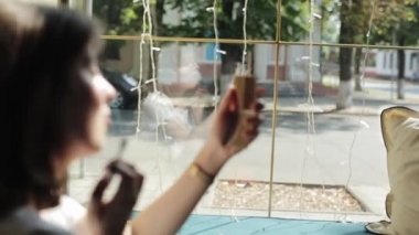 Nazik genç bir kız pencerenin yanındaki bir kafede oturur ve elinde ayna tutarak makyajını yapar. Yan görüş. Yakın plan. Ön planda bulanıklık. Penceredeki yansımaya odaklan
