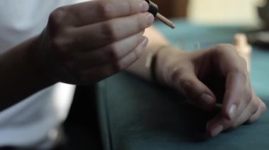 Beyaz tişörtlü genç bir kadın bir masada oturuyor ve eline kavanozdan fondöten sürüyor. Elleri yakın çekim. Bulanık arkaplan