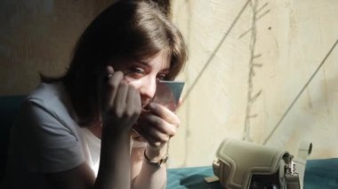 Çekici genç bir kız el çantasıyla bir masanın penceresinde oturur ve küçük bir aynaya bakarken göz kalemi yapar. Ön manzara. Yakın plan.