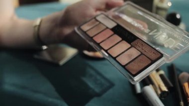 Misk, Belarus - 25 Ağustos 2020: Fırçalı genç bir kız diğer kozmetik ürünlerinin arka planında makyaj için paletten gölgeler topluyor. Elleri yakın çekim. Kamera odağı değiştirir.