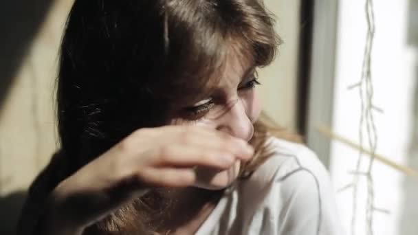 Retrato de una joven gentil con maquillaje ligero en el fondo de la ventana y se ríe alisándose el cabello. Vista frontal — Vídeo de stock