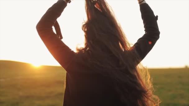 Een schattige jonge vrouw straalt haar lange haar tegen de zonsondergang en gaat weg met haar rug gekeerd. Langzame beweging — Stockvideo