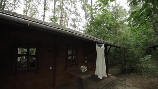 Prepararsi per una cerimonia nuziale in una tenuta di campagna. Il vestito da sposa pende da un appendiabiti all'ingresso della casa in legno — Video Stock
