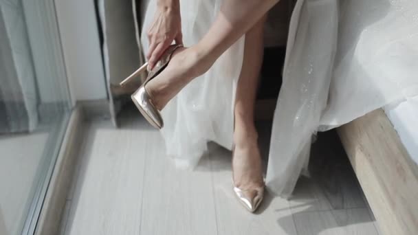 Close-up de pernas de uma jovem noiva vestindo belos sapatos de salto alto de ouro enquanto se prepara para uma cerimônia de casamento — Vídeo de Stock