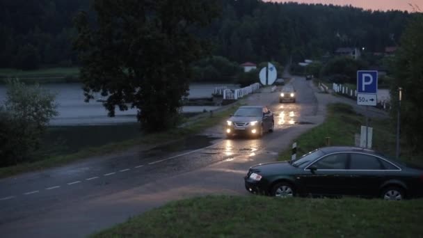 Gomel, Fehéroroszország - Augusztus 28, 2020: Autók a fényszórók a meghajtó egy híd mellett egy nagy tó egy nedves úton eső — Stock videók