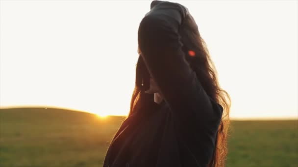 Una giovane donna adorabile raddrizza i capelli lunghi contro il tramonto e se ne va con la schiena girata. Rallentatore — Video Stock