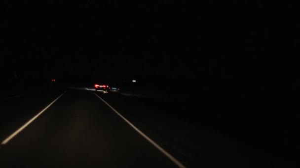 Una vista desde la cabina de un coche de paso en un coche de policía con luces intermitentes de pie en el lado de la carretera de la noche — Vídeos de Stock