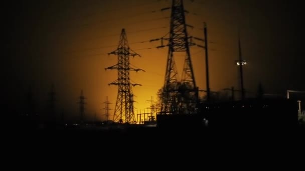 Torens van elektriciteitsleidingen en draden tegen de achtergrond van oranje licht aan de nachtelijke hemel vanuit het raam van een passerende auto — Stockvideo