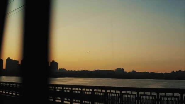 Autos fahren langsam über die doppelte Brücke vor dem Hintergrund von Sonnenuntergang und Silhouetten von im Bau befindlichen städtischen Gebäuden — Stockvideo