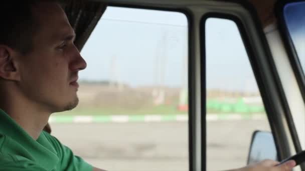 Um jovem com uma camiseta verde dirige seu carro e olha para a estrada com concentração quando passa pelo posto de gasolina. Dentro da cabina — Vídeo de Stock