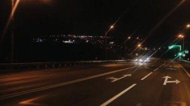 Trafik yoğun bir gece yolunda trafik ışıkları ve uzaktaki şehir ışıklarının görüntüsü ile kavşakta. Yolculuk