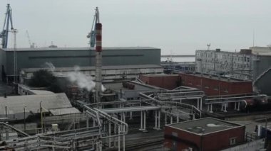 Petrol endüstrisinin petrol rafinerisinin geniş bir bölgesi. Boru hatları ve deniz arka planında kule vinçleri var.