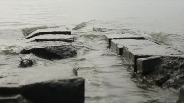 Large concrete slabs of breakwater surrounded by water on the seashore and waves roll over them — Αρχείο Βίντεο