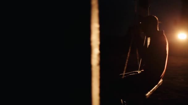 一个年轻人在黑暗中站在一辆货车的前灯上，在明亮的开关的背景下，骑着绳子摆动着。慢动作 — 图库视频影像