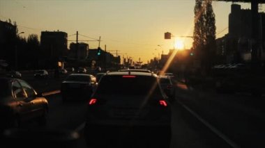 Rostov-on-Don, Rusya - 17 Eylül 2020: Arabalar yoğun bir şehir yolu boyunca gün batımının arka planına ve binaların siluetlerine doğru sürüyorlar ve trafik ışıklarında duruyorlar