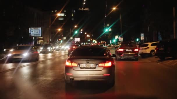 Rostov-sur-le-Don, Russie - 17 septembre 2020 : Des voitures circulent le long de la route dans la ville la nuit et passent par des rangées d'automobiles stationnées près de divers établissements. La caméra change de focus — Video