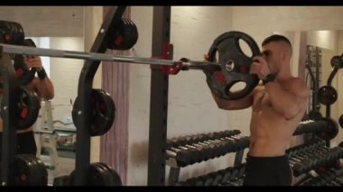 Siyah spor şortlu genç kaslı sporcu spor salonunda antrenman yapıyor ve güç egzersizleri için halterlere gözleme asıyor.