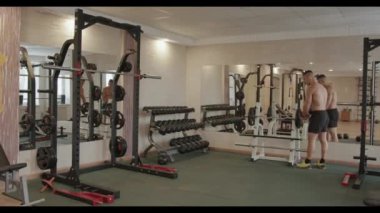 Siyah spor şortlu genç vücut geliştirici spor salonundaki halterlere krep asar ve egzersiz rafından bir halter alır.