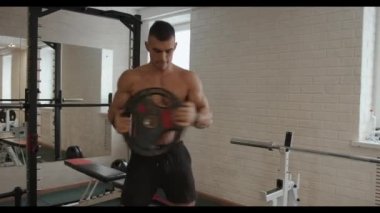 Genç ve güçlü bir adam spor salonunda antrenman yapıyor ve ellerinde krep halteriyle karın kaslarını şişiriyor.