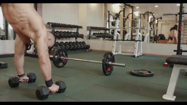 Jeune homme fort en short de sport noir s'entraînant dans la salle de gym et faisant un handstand appuyé sur de gros haltères métalliques — Video