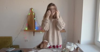 Neşeli genç bir kadın Noel ve yeni yıl için mutfakta köpeğiyle zencefilli ekmek hazırlıyor ve gözlüğü gibi kurabiye kesicilerle takılıyor. Yavaş çekim