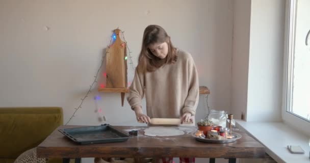 Jovem encantadora lança massa de gengibre para o Natal e Ano Novo em uma mesa de madeira com uma composição com velas acesas — Vídeo de Stock