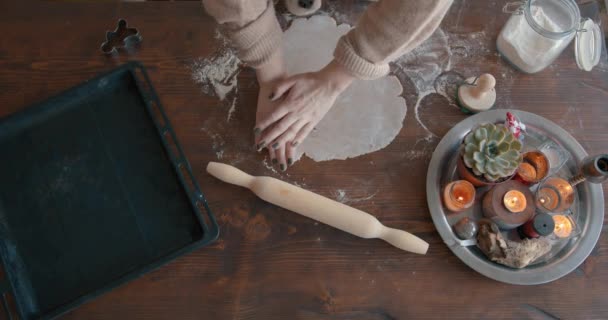 Uma jovem corta as estatuetas do pão de gengibre de Natal com moldes em uma mesa de madeira com uma composição de velas acesas. Vista de cima. Close-up de mãos — Vídeo de Stock