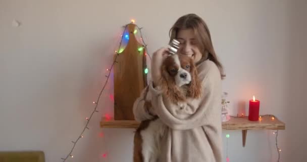 Cheerful young girl cooking gingerbreads for Christmas and dances with her dog in her arms against the background of garland and candles — Stock Video