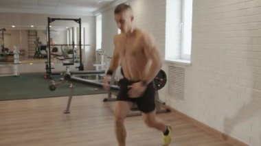 Genç kaslı adam spor salonunda antrenman yapıyor, mindere uzanıyor, mekik çekiyor, kalçalarını kaldırıyor, karın kaslarını ve kalçalarını şişiriyor.