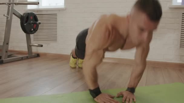 Młody muskularny mężczyzna w czarnych spodenkach sportowych ćwiczy na siłowni i rzuca się ze skokami pompując quady i pośladki — Wideo stockowe