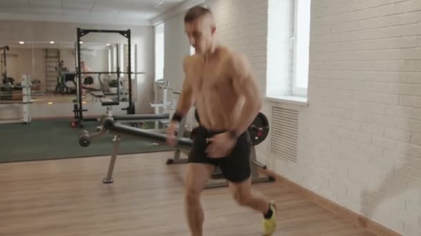 Joven musculoso entrenando en el gimnasio y acostado en la esterilla haciendo abdominales y levantando las caderas bombeando los abdominales y las nalgas — Vídeo de stock