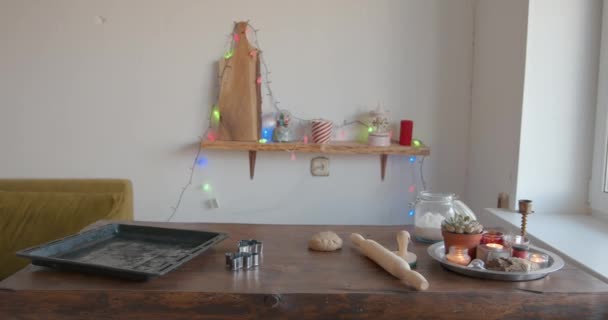 Masa de pan de jengibre para las vacaciones de Navidad y cortadores de galletas de metal se encuentran en una mesa de madera con textura en la cocina decorada con velas y guirnaldas — Vídeos de Stock