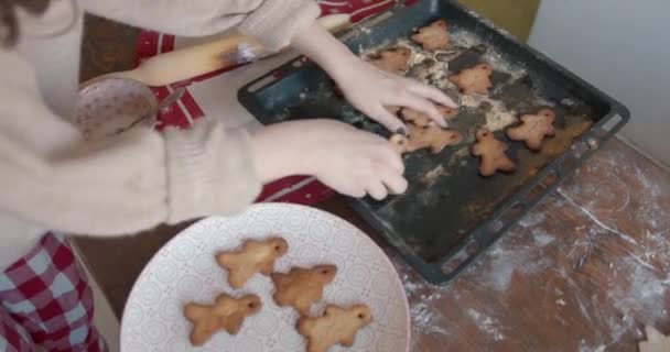 A young girl takes it out of the oven gingerbreads for Christmas and New Year in the shape of a spruces and little men and puts them on a large dish