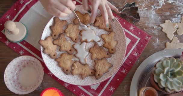 Un lindo perro se encuentra con su bozal en la mesa y observa como una niña decora el pan de jengibre con esmalte para Navidad y Año Nuevo. Vista desde arriba — Vídeos de Stock