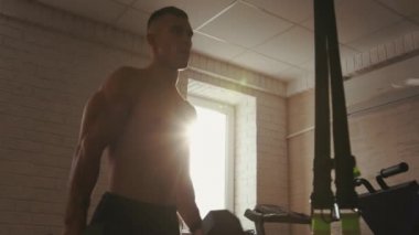 Genç kaslı adam spor salonunda antrenman yapıyor ve leğen kemiğini yere değdirme egzersizinde farklı yönlere çeviriyor.