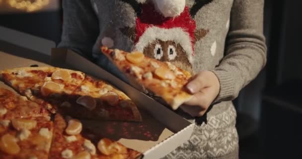 Młoda dziewczyna w swetrze z świątecznym jeleniem trzyma pudełko po pizzy z kawałkami kurczaka i mandarynkami w dłoniach. — Wideo stockowe