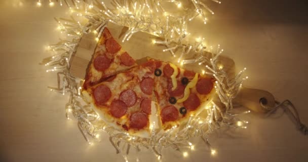 Gros plan d'une tranche de pizza perperperoni dans la main des filles sur un fond de lumières floues d'une guirlande — Video